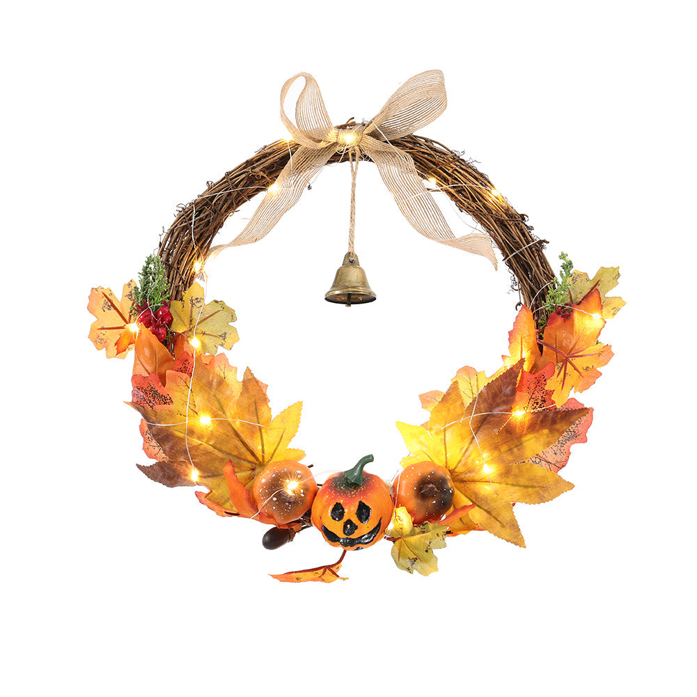 Open woven branch harvest wreath with maple leaves, carved-face pumpkins, a burlap bow and a bell on white