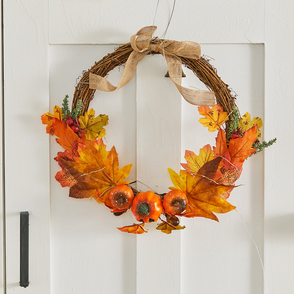 The open harvest wreath with a burlap bow and bell hanging on a white door
