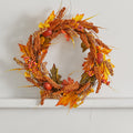 Artificial autumn wreath of orange sorghum, maple leaves, red berries and small red fruits on a white wall
