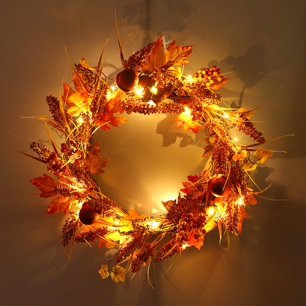 Autumn sorghum and maple leaf wreath glowing with warm LED lights against a dark wall