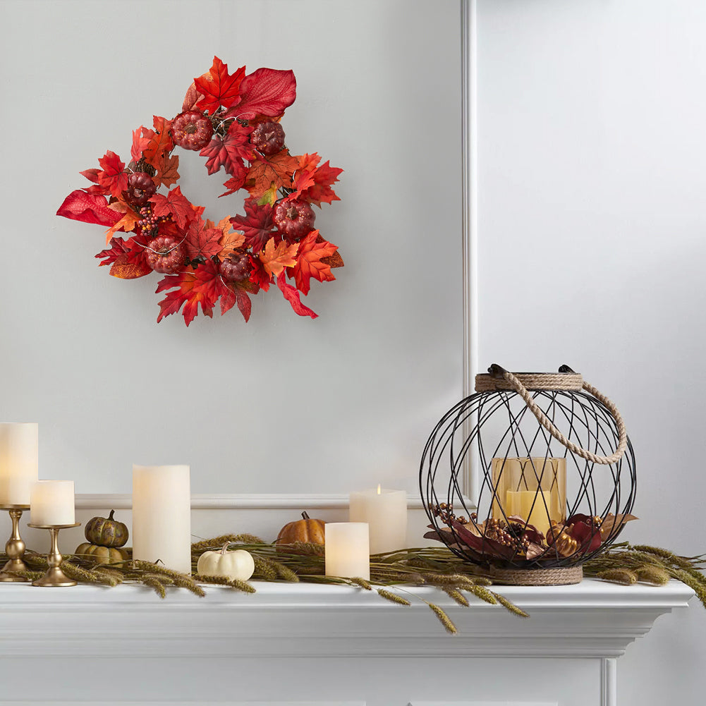Red maple leaf and pumpkin wreath on a grey wall above a white mantelpiece with candles and a lantern