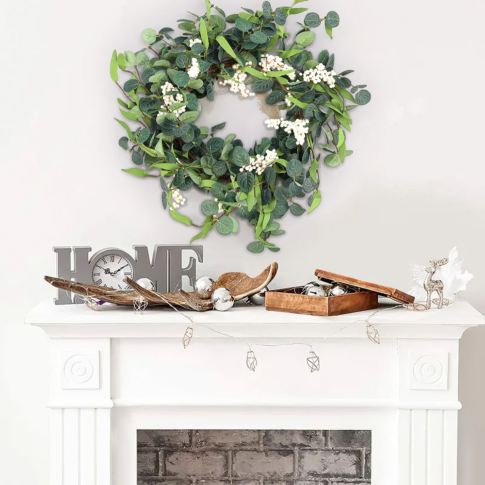 Eucalyptus wreath with white berries hanging on a white wall above a white fireplace