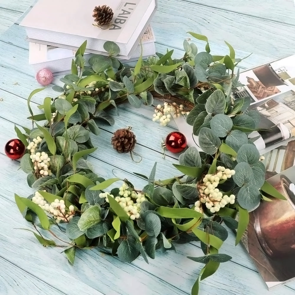 Eucalyptus wreath with white berries on a pale blue wooden table among books, pine cones and baubles