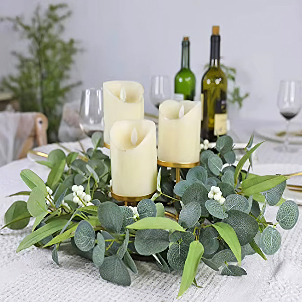 Eucalyptus wreath lying on a dining table as a ring around three cream pillar candles