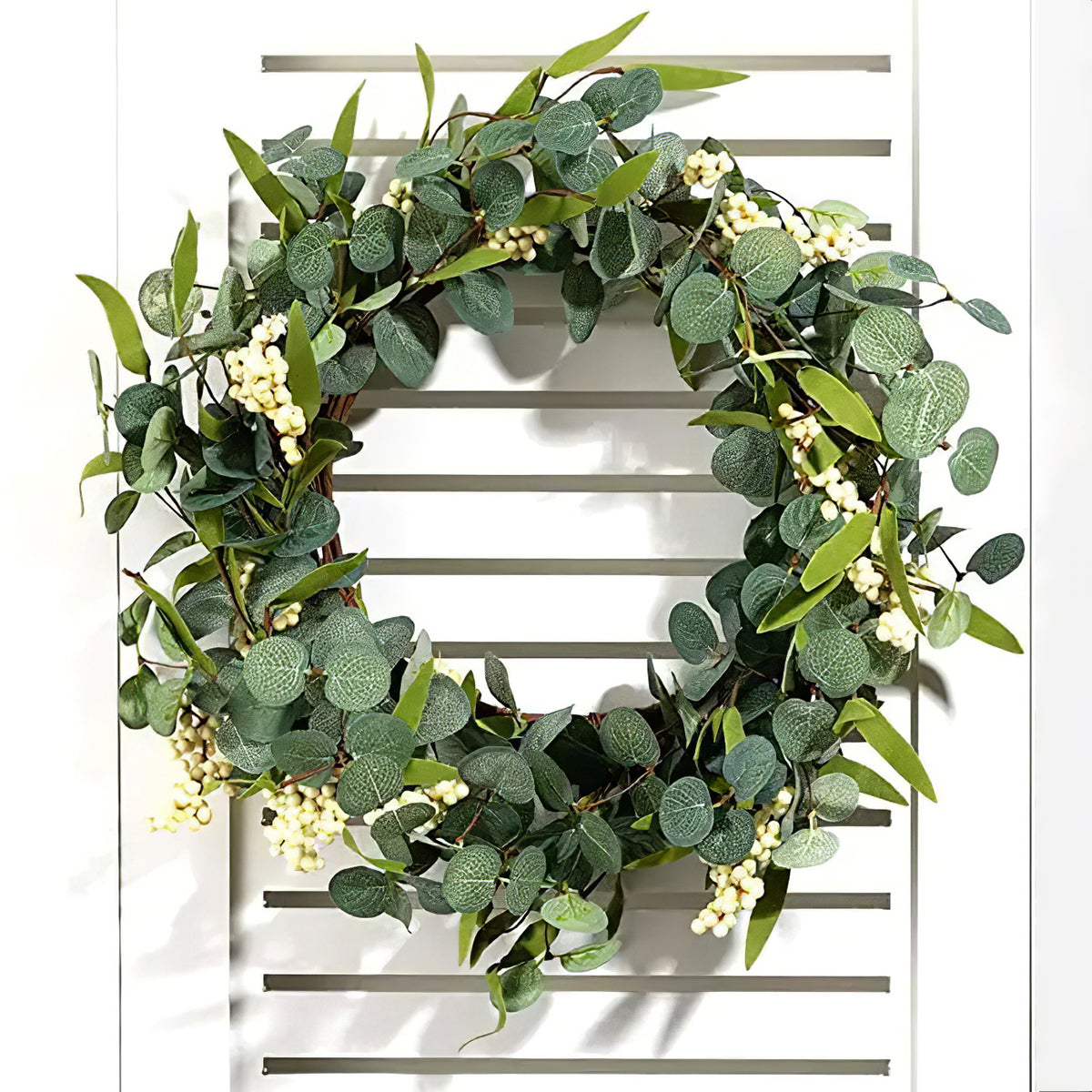 Artificial eucalyptus wreath with white berries hanging on a white slatted shutter