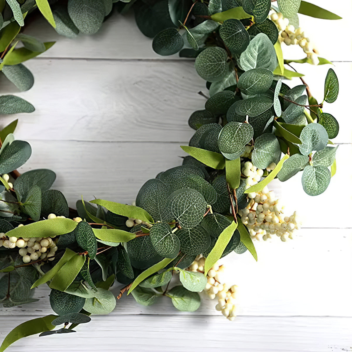 Close view of the wreath's round eucalyptus leaves and white berry clusters against white boards