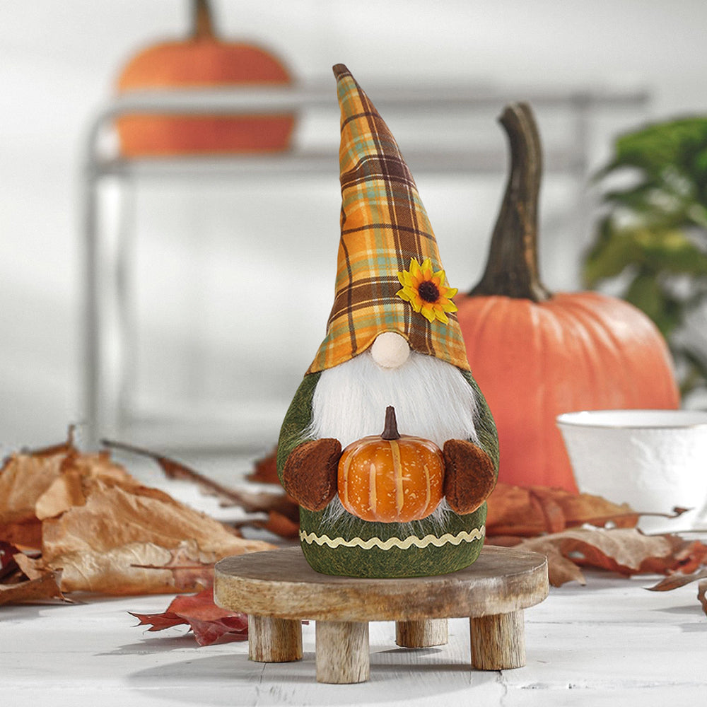 Autumn gnome with an orange plaid hat and sunflower holding a pumpkin, on a small wooden stand beside a pumpkin
