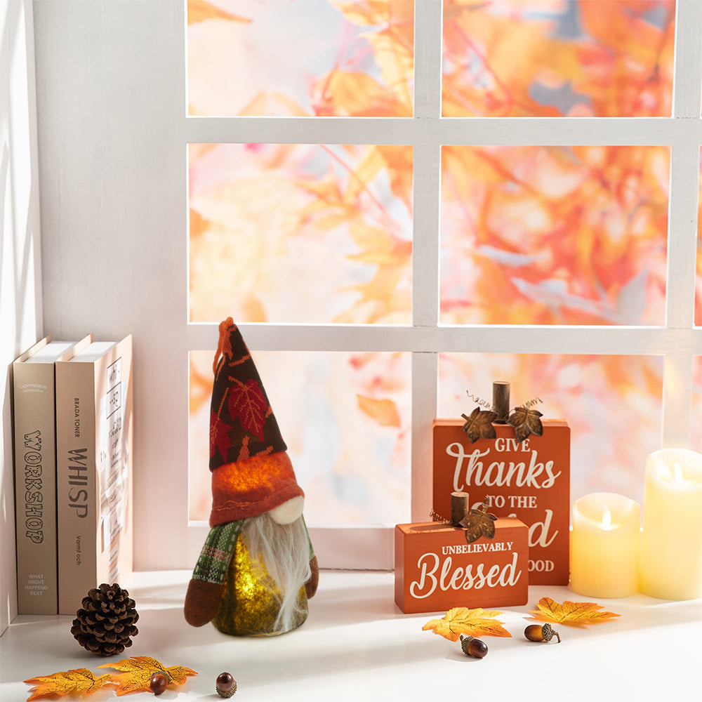 Autumn gnome with a maple-leaf hat glowing on a white windowsill beside books, candles and autumn leaves