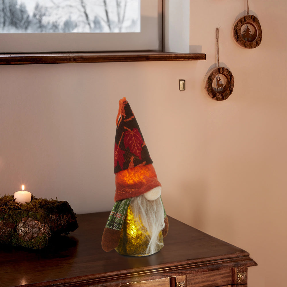 Lit autumn gnome standing on a dark wooden sideboard beside a candle