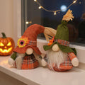 Two autumn gnomes, one in an orange hat with a sunflower and one in a green hat, on a white windowsill