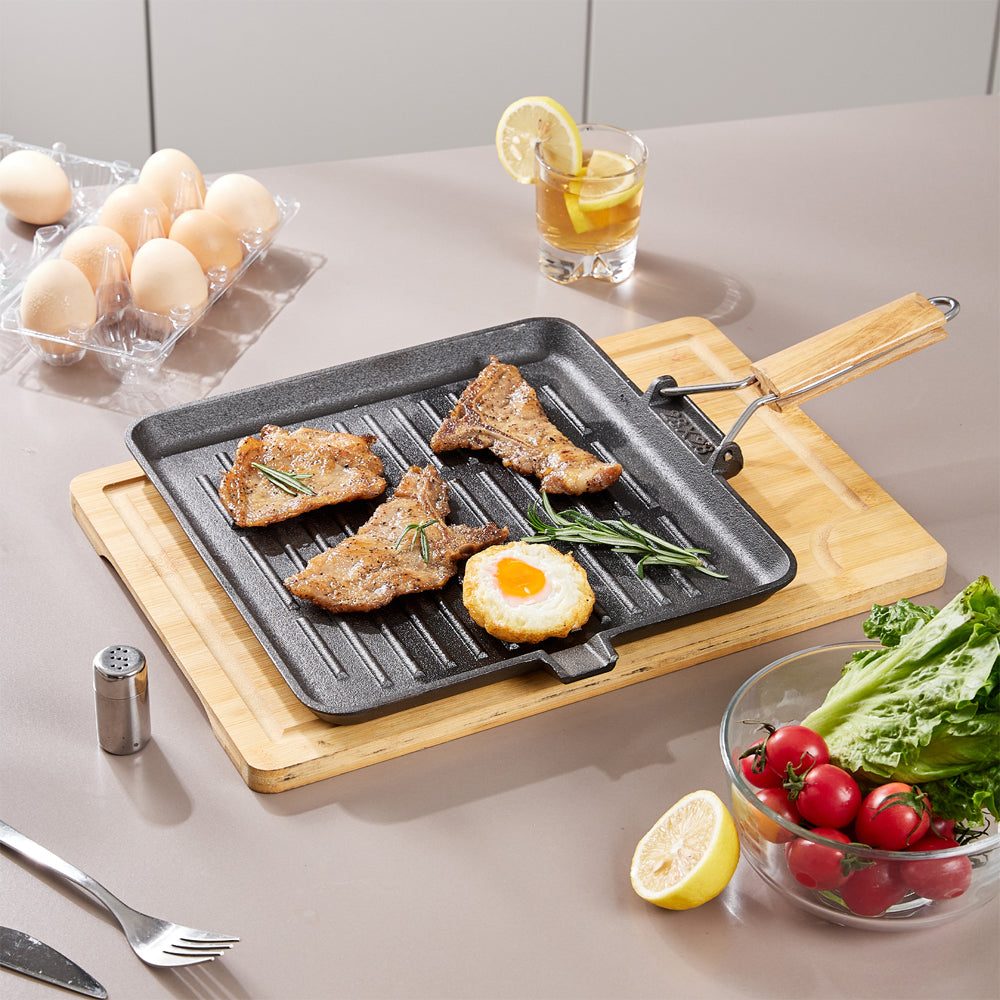Square cast iron grill pan with steaks and a fried egg on a bamboo board