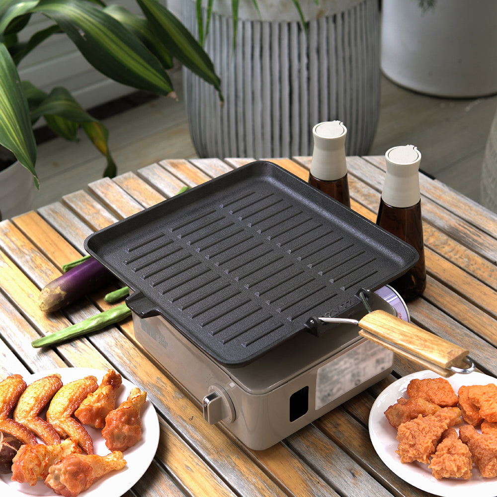 Square grill pan on a portable camping stove on an outdoor table with chicken wings