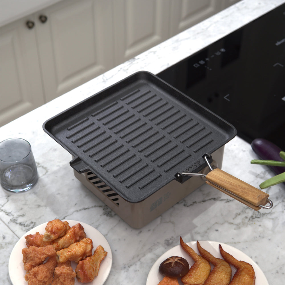Square grill pan on a portable stove on a marble worktop beside plates of chicken