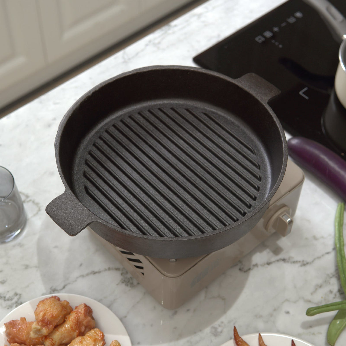 Empty ribbed cast iron grill pan on a beige camping stove on a marble worktop