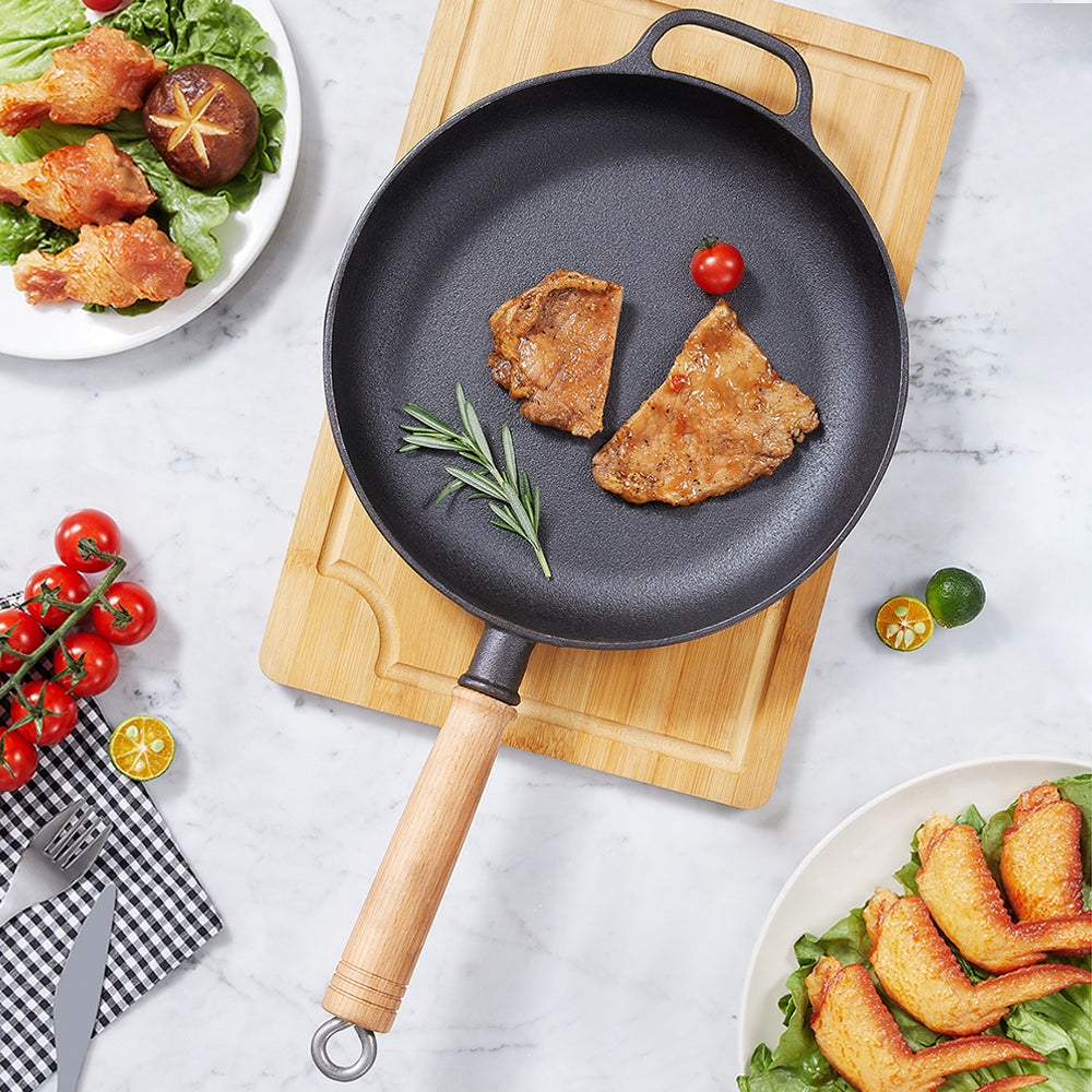 Top view of the cast iron skillet with two pork cutlets on a bamboo board, wooden handle with a metal ring