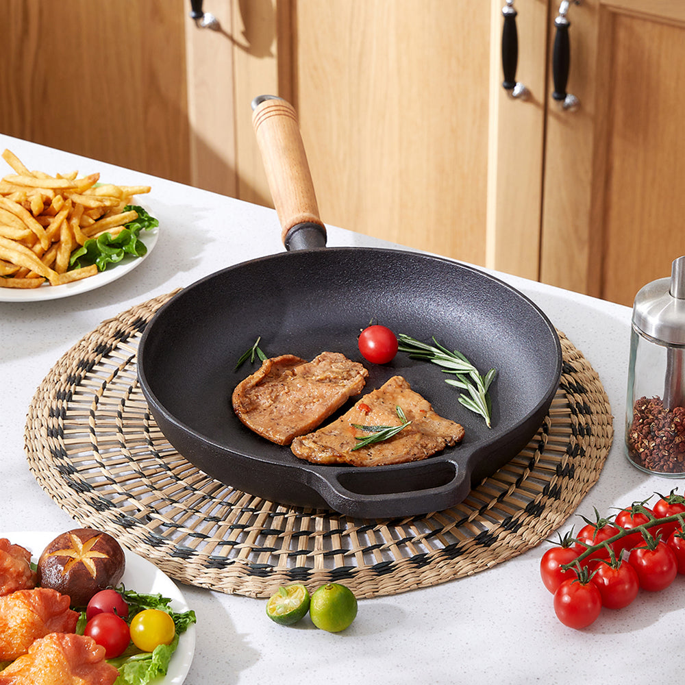 Cast iron skillet with cutlets and a tomato on a woven mat, helper loop to the front
