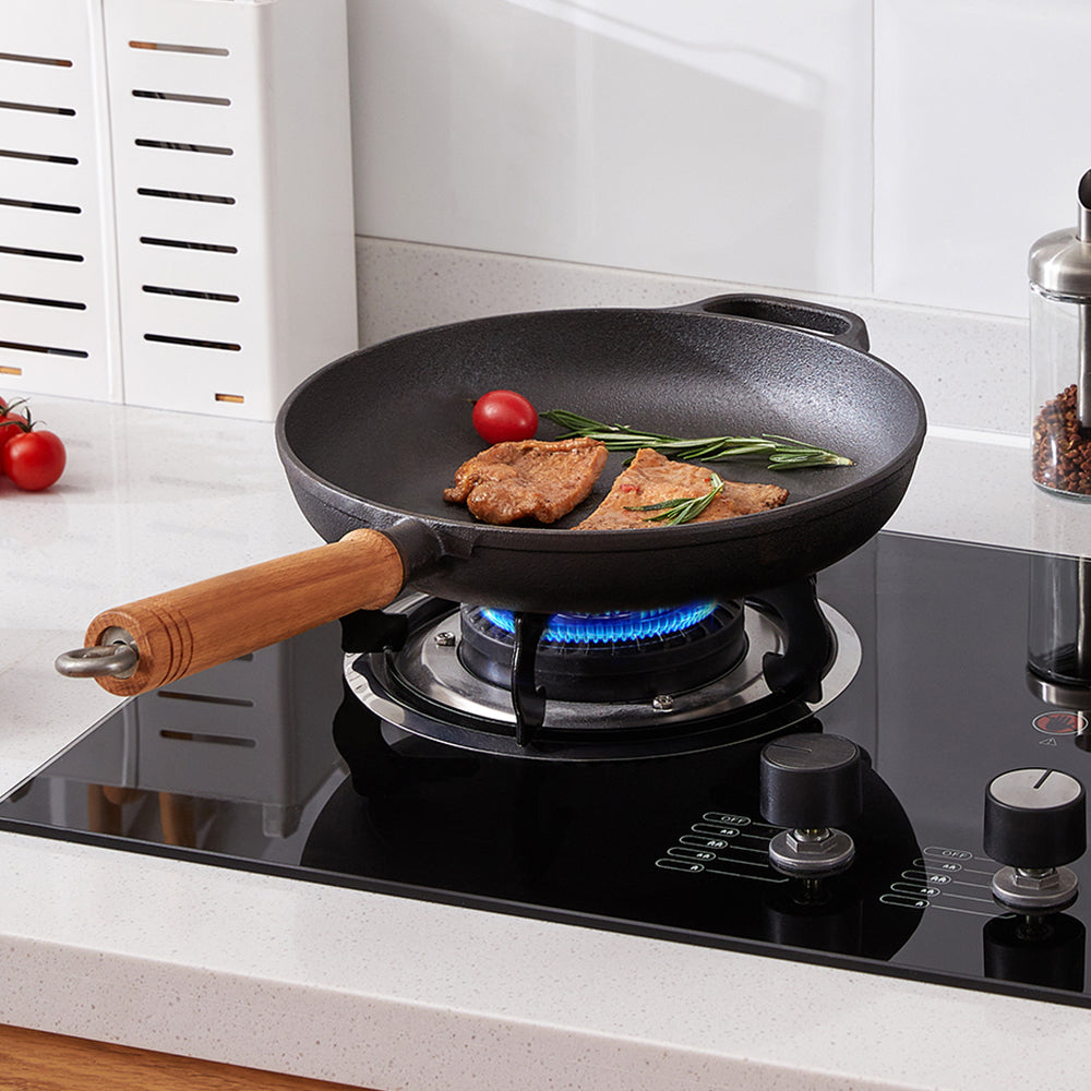 Cast iron skillet with pork and rosemary on a lit gas hob, its wooden handle to the front