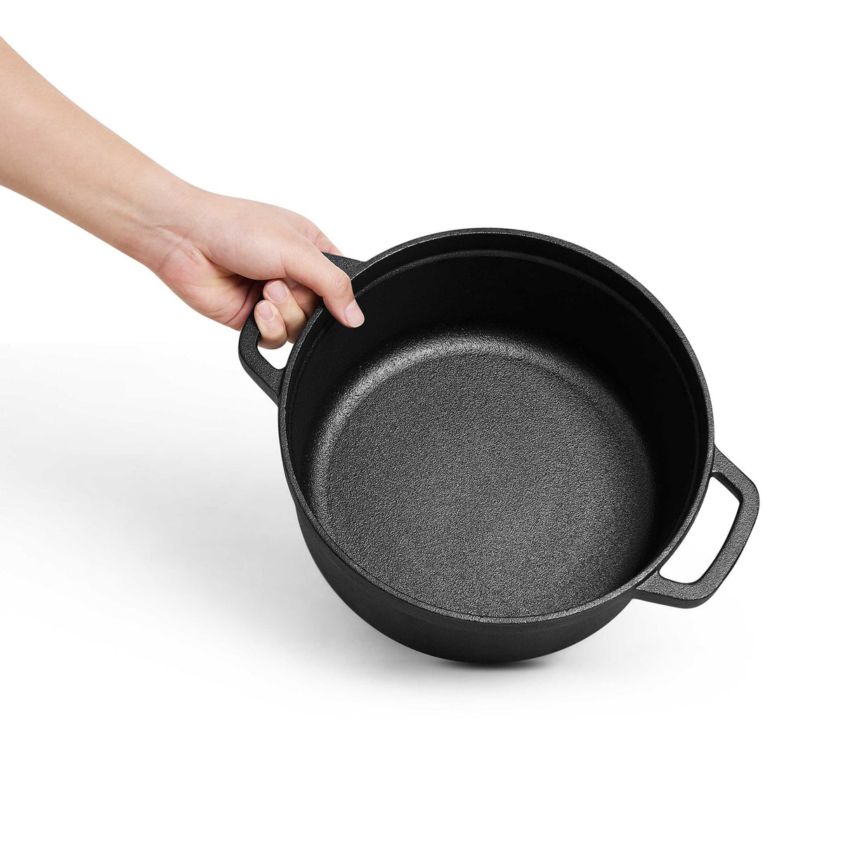 A hand holding the empty cast iron pot by one loop handle on a white background