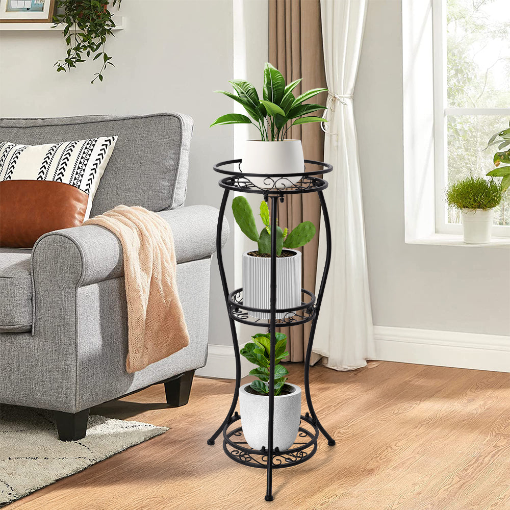 Three-tier iron plant stand with potted plants beside a grey sofa in a living room