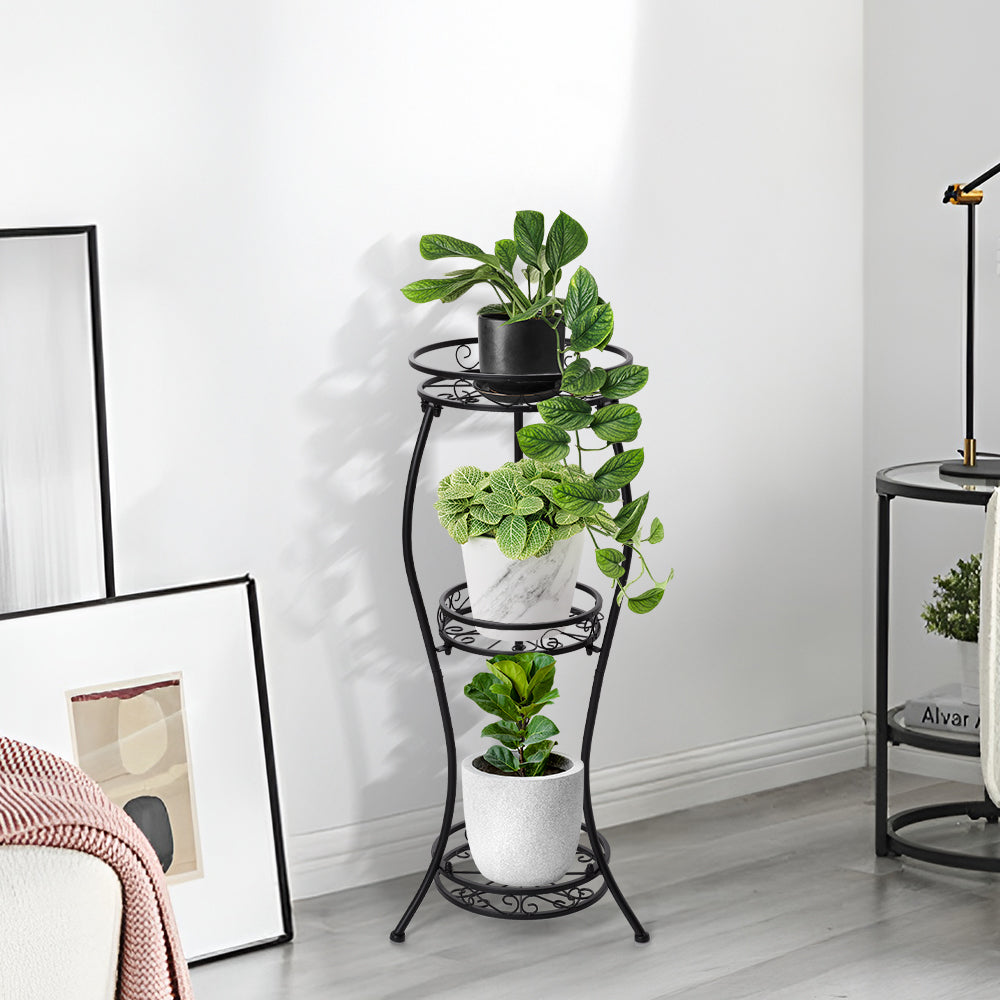Black iron plant stand holding three pots of trailing plants in a white room
