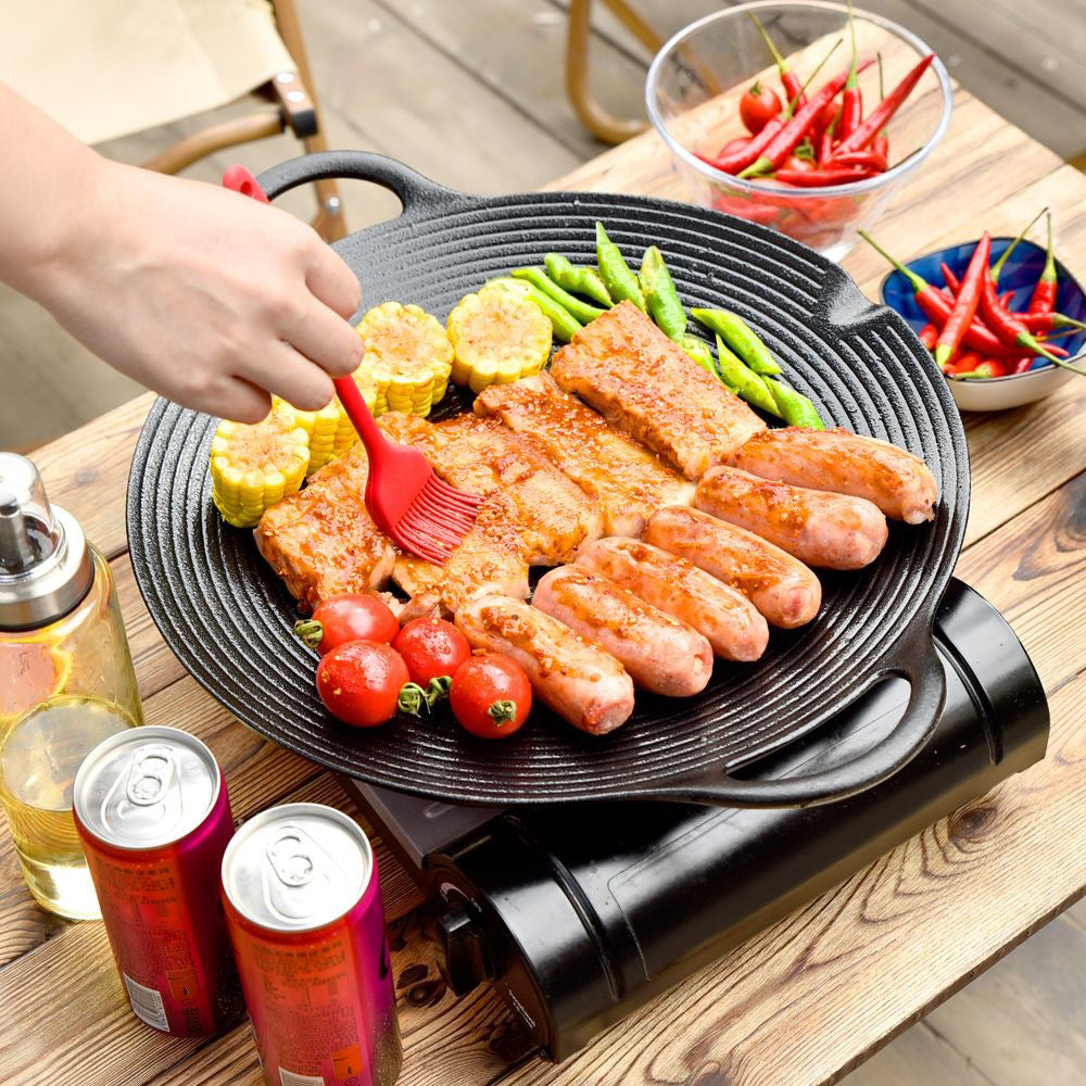 Sausages, pork, corn and tomatoes grilling on the cast iron pan outdoors, brushed with oil