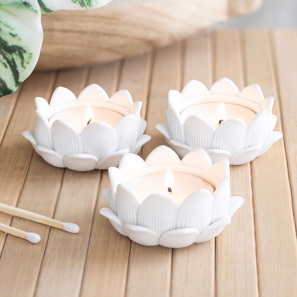 Three white lotus flower tealight holders with lit tealights on a wooden table