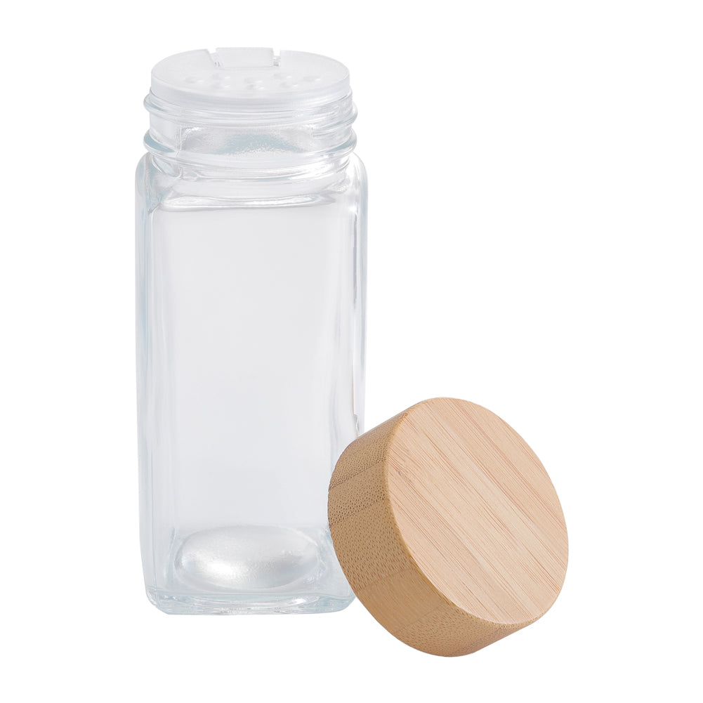 Empty square glass jar with its sifter insert beside a round bamboo lid, on white