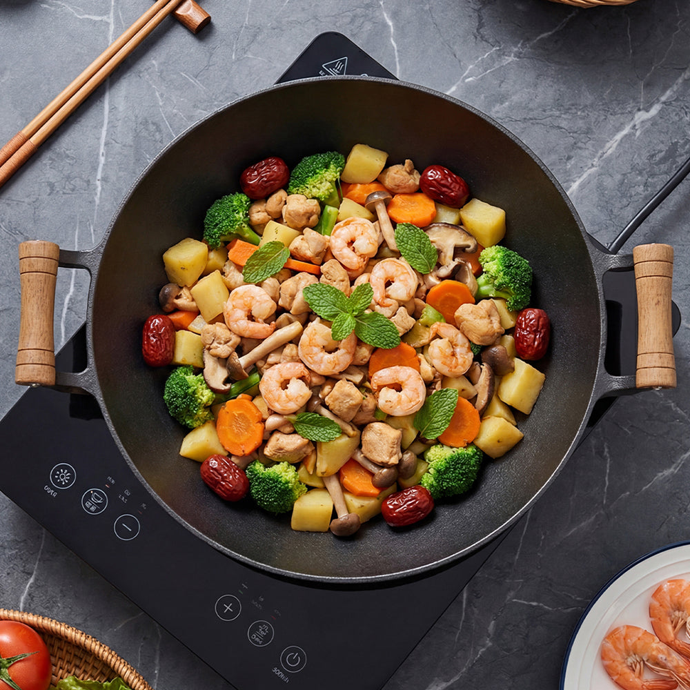Top view of the cast iron wok filled with prawns and vegetables on a black glass hob