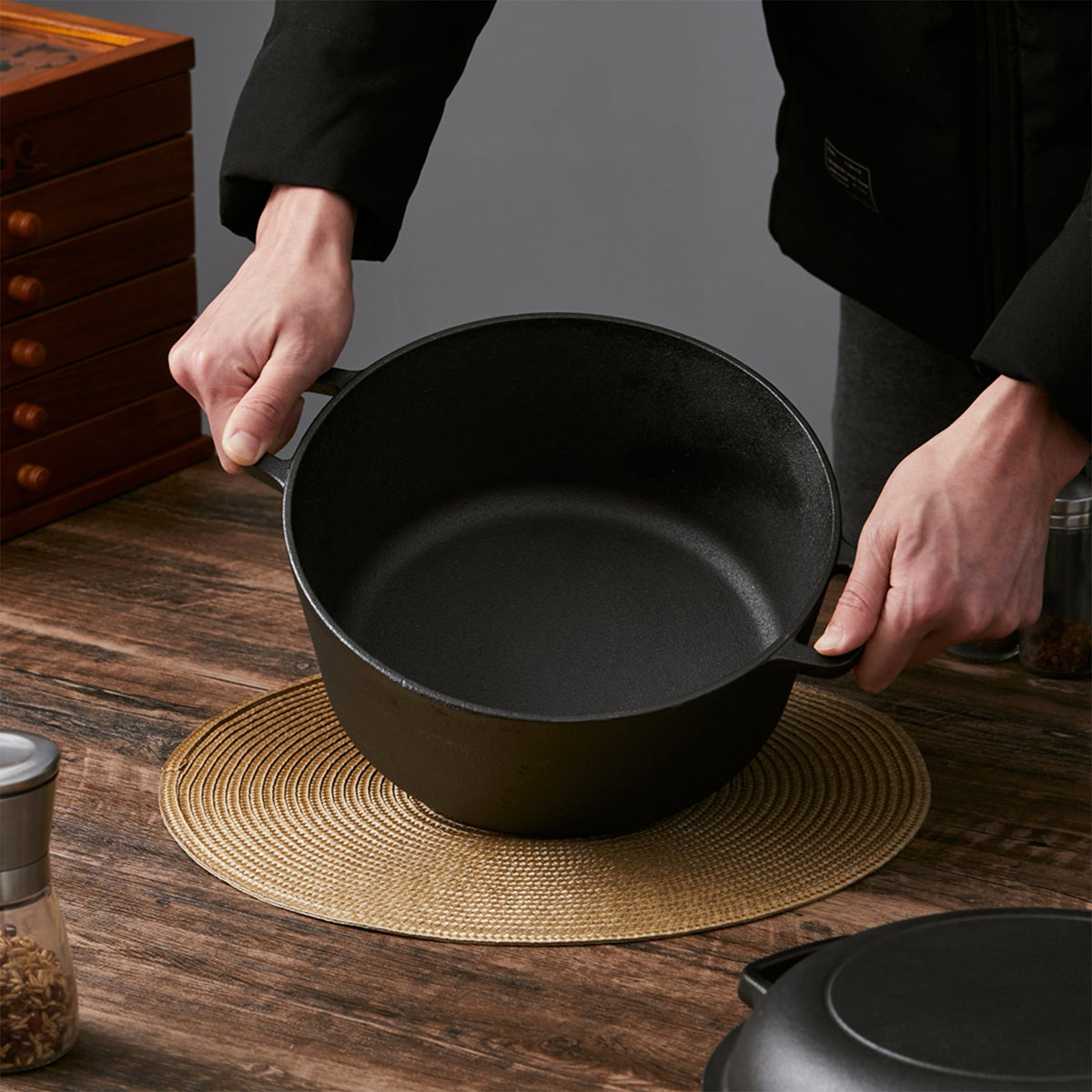 Two hands lifting the empty cast iron pot by its loop handles over a woven mat