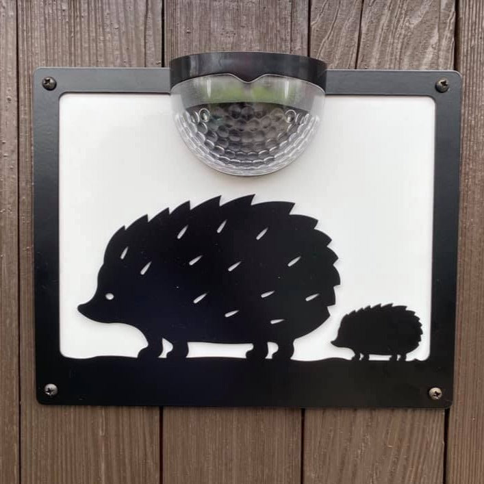 Hedgehog solar wall plaque with white backing panel on a wooden fence