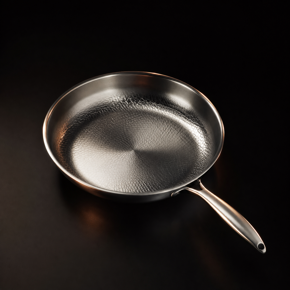 A hammered titanium frying pan photographed at an angle on a black surface, its long tubular handle to the right.