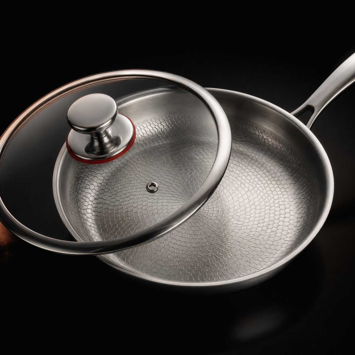 The same pan with its clear glass lid tilted against the rim, showing the lid's steam vent and metal knob on a red seal.
