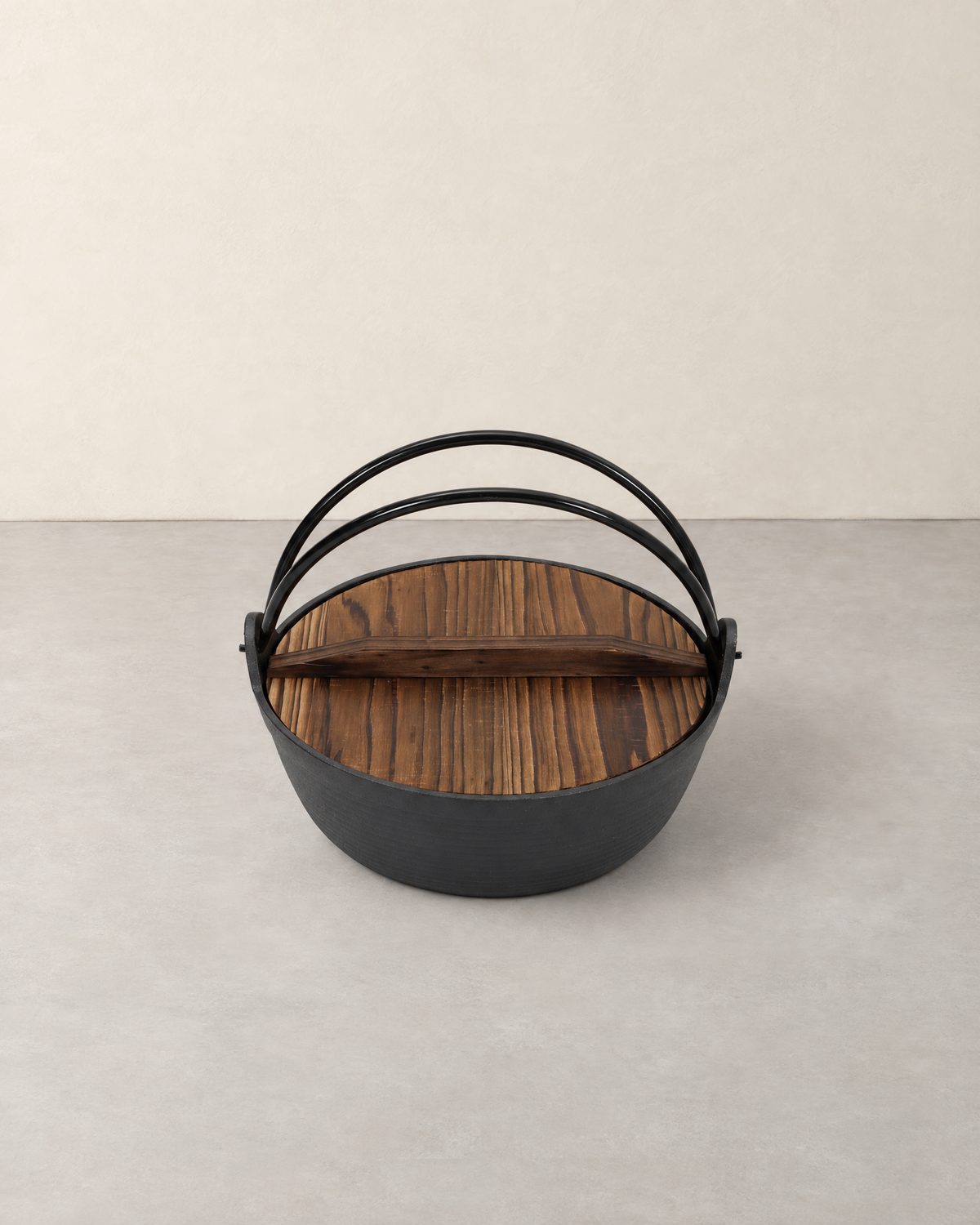 Black cast iron nabe pot with a brown wooden lid and two arched metal handles