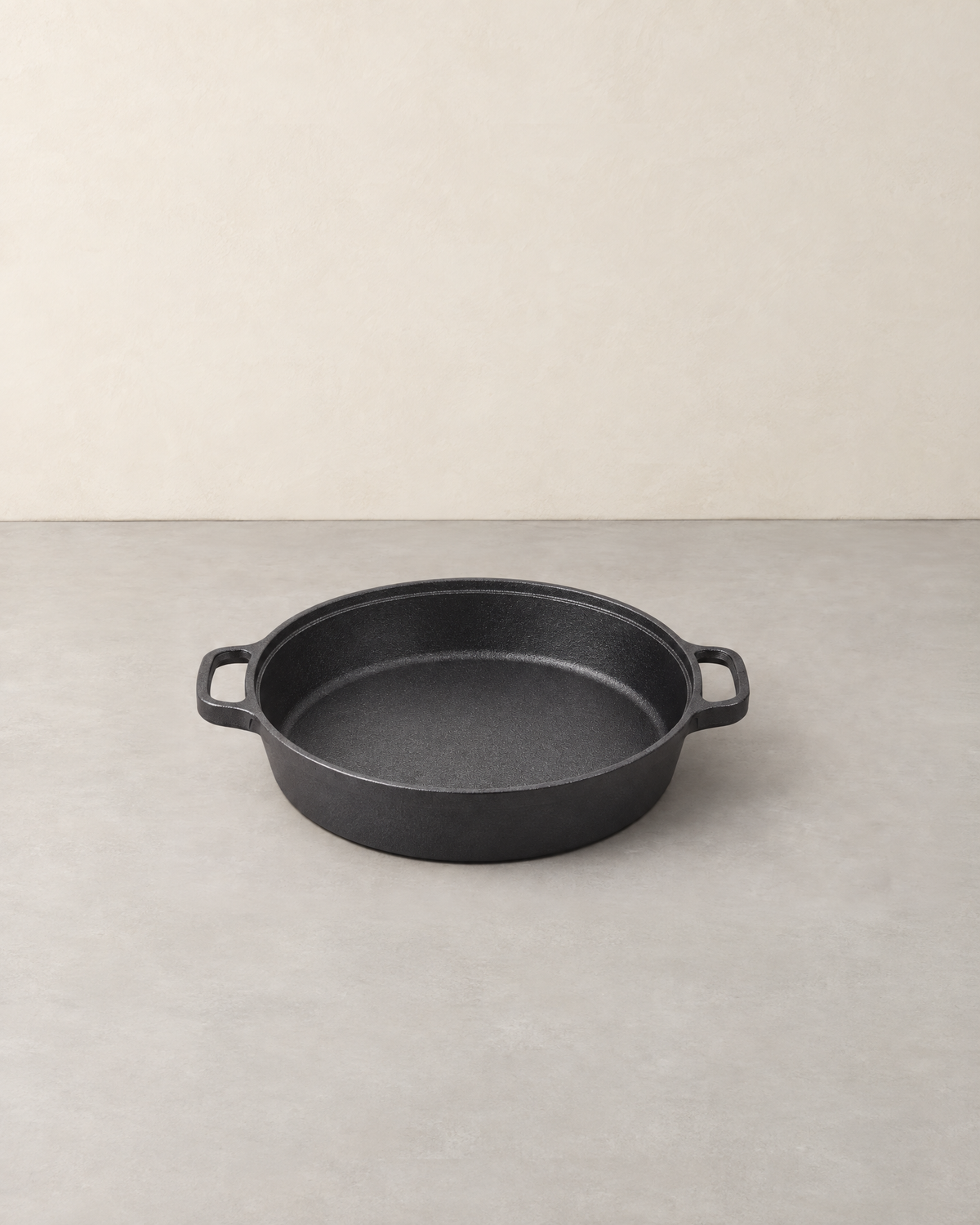 Deep round black cast iron skillet with two side loop handles, empty