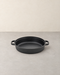 Wide shallow black cast iron skillet with two side loop handles on a pale concrete floor