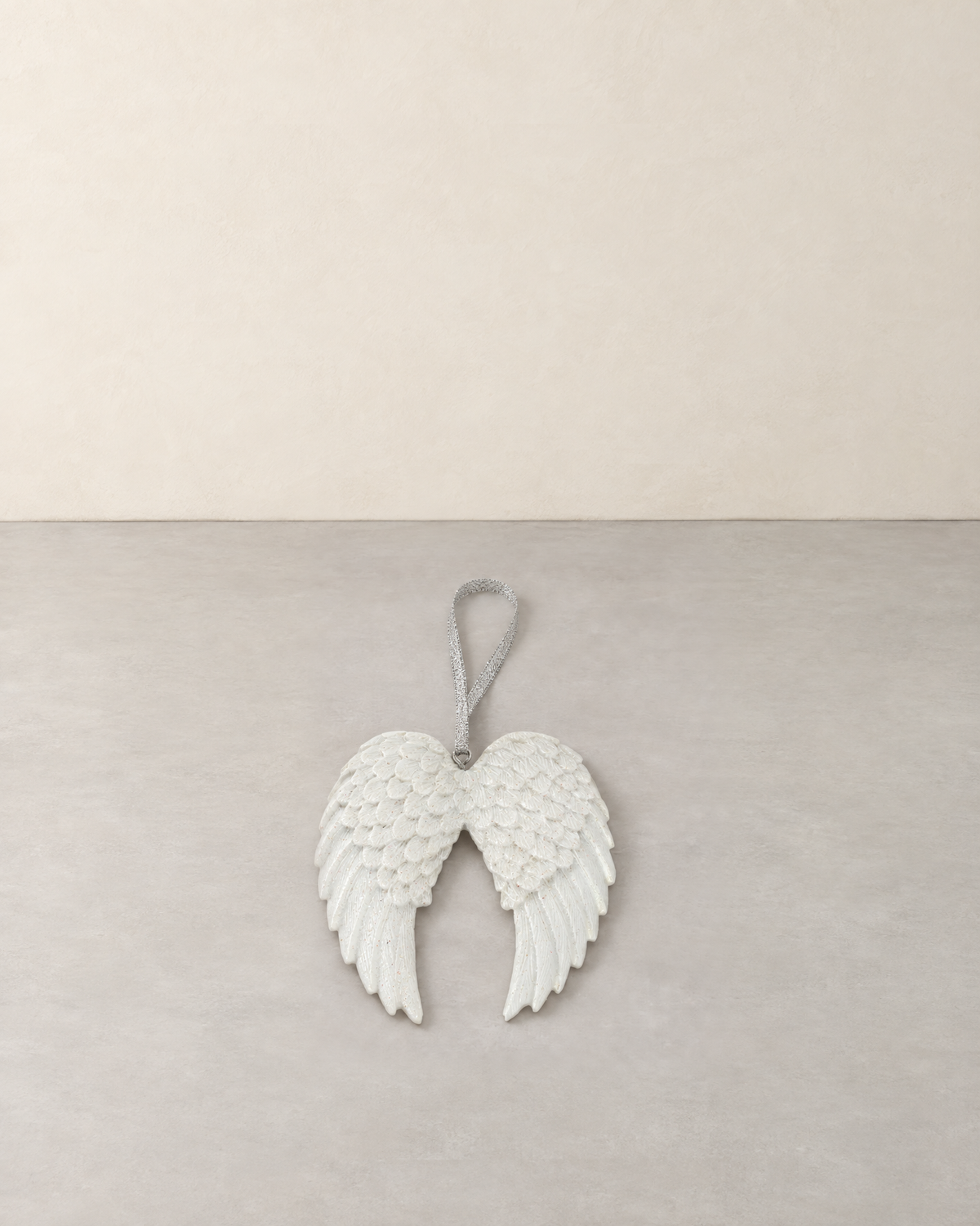 White double angel wing decoration with glitter feathers and a silver ribbon, lying flat