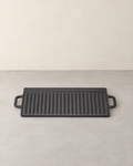 Black rectangular cast iron griddle with its ribbed side up and a loop handle at each end