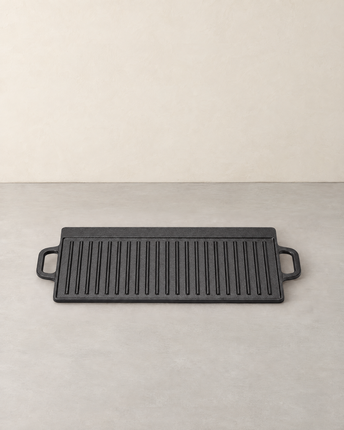 Black rectangular cast iron griddle with its ribbed side up and a loop handle at each end