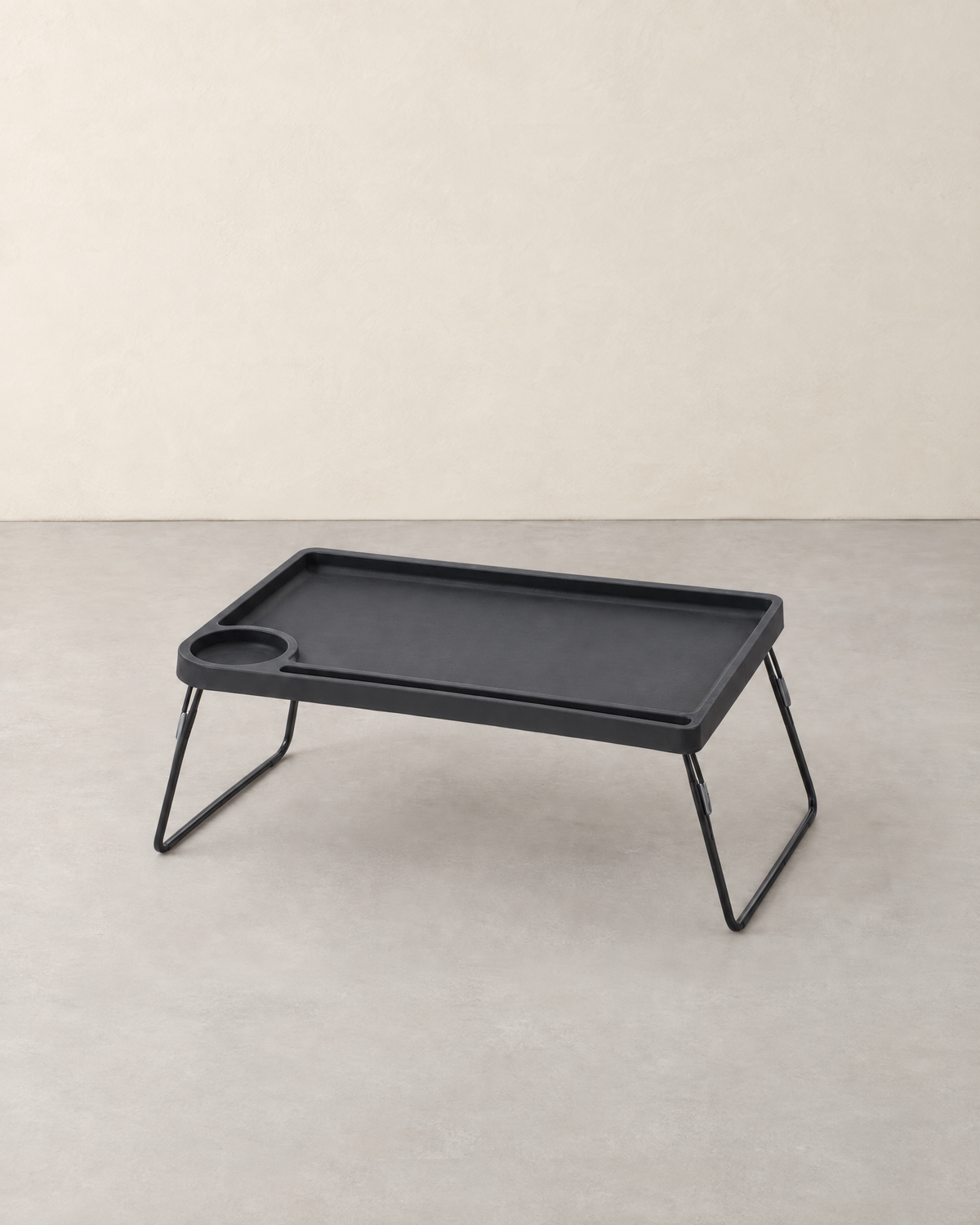 Black folding bed table with a raised rim, cup holder and tablet groove on thin metal legs