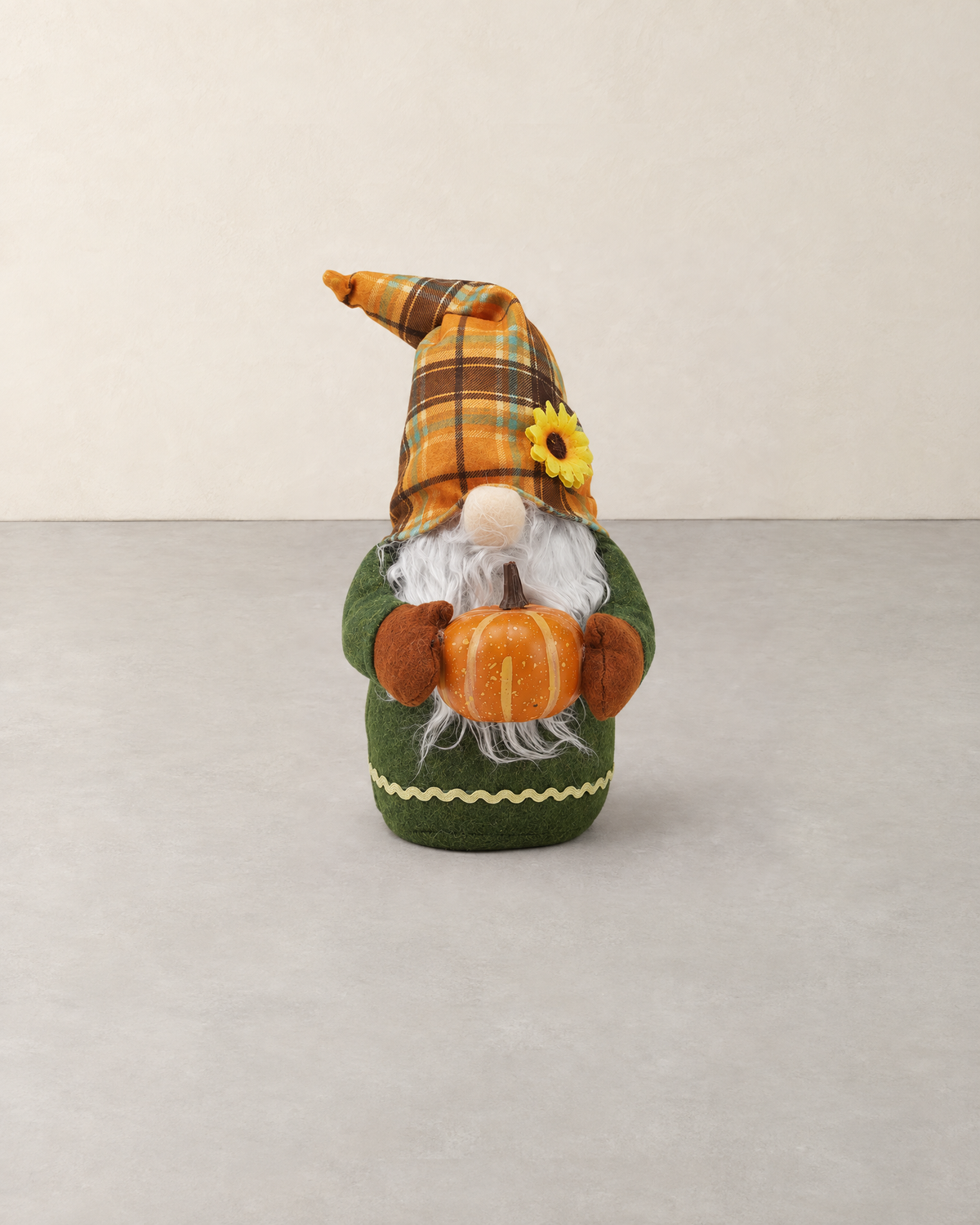 Autumn gnome in an orange plaid hat with a sunflower, holding a pumpkin, standing on a pale grey floor against a cream wall