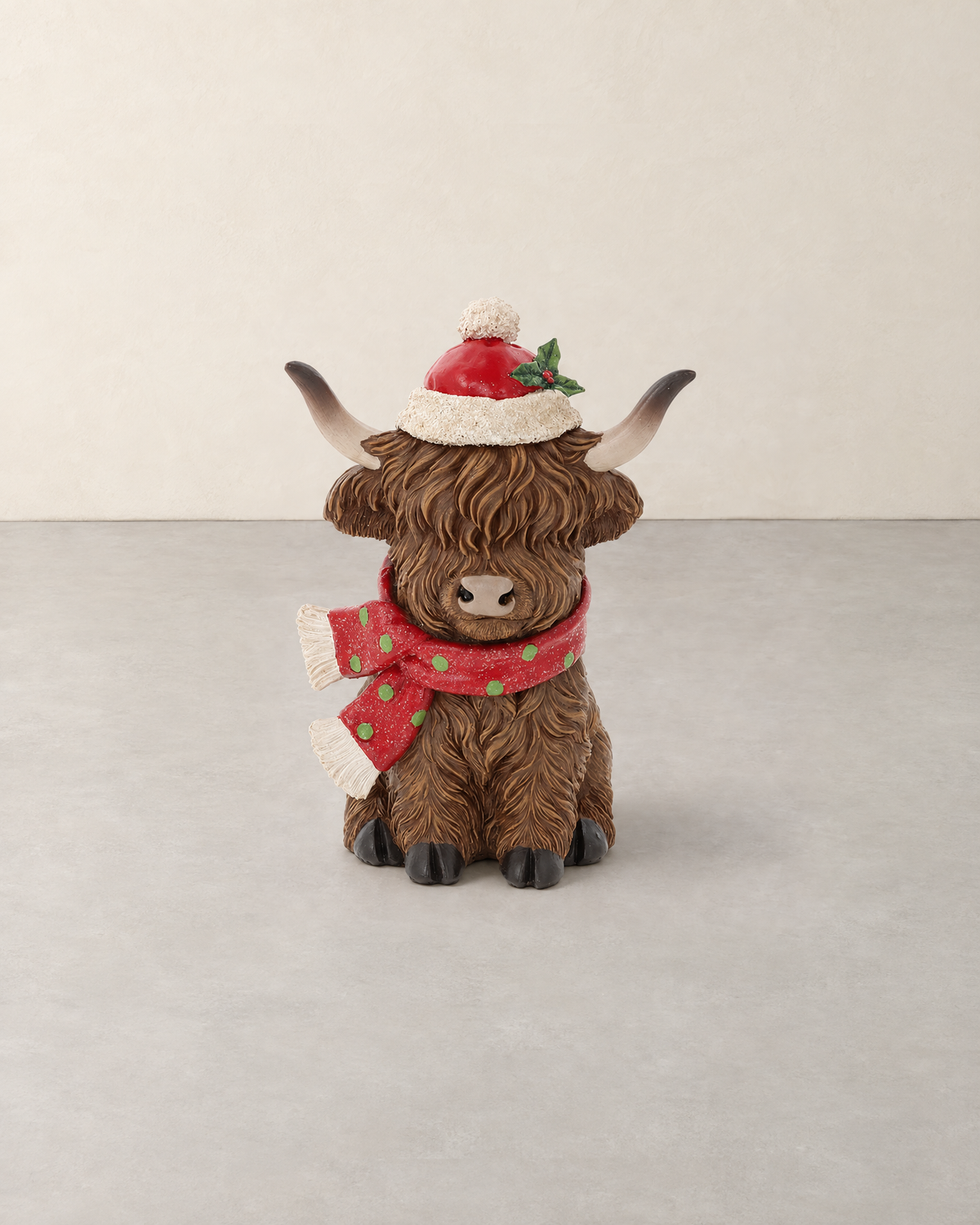 Sitting Highland Cow figure in a red Santa hat and a red scarf with green dots