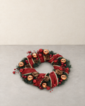 Christmas wreath with red glitter ribbon, copper baubles and pine cones lying on a pale grey floor against a cream wall