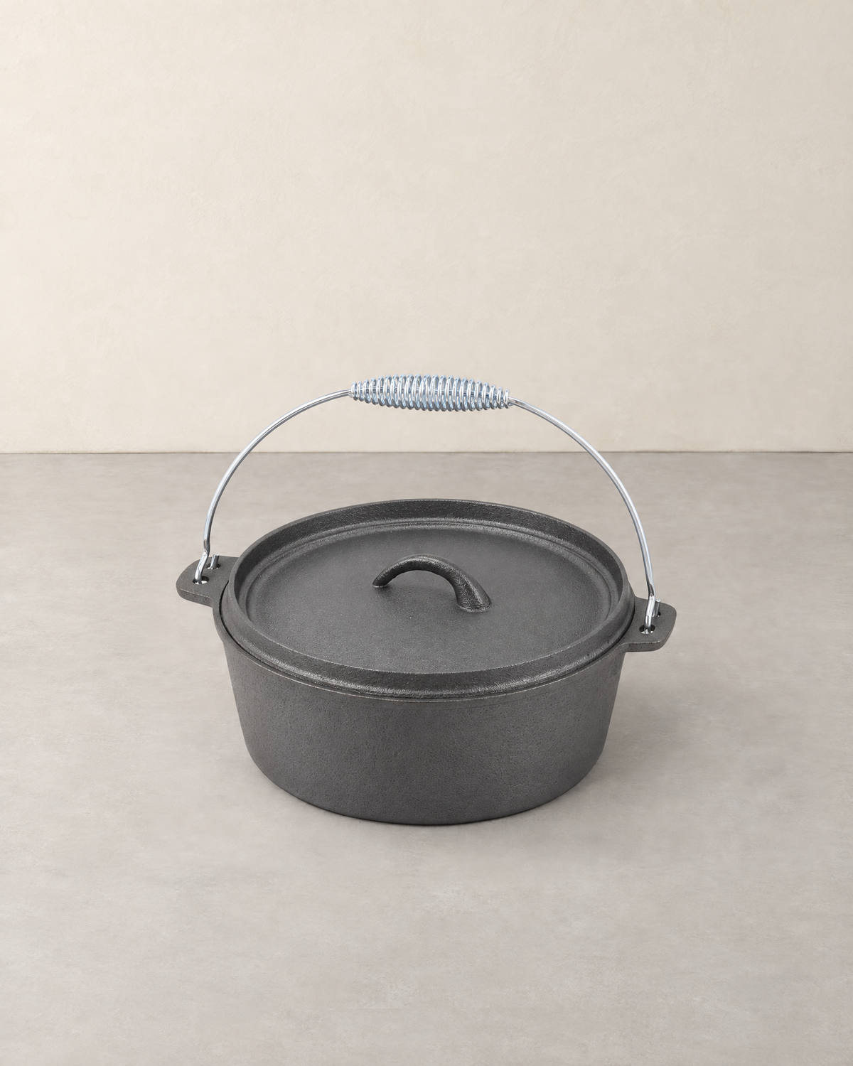 Round cast iron camping Dutch oven with flat lid and a silver wire bail handle with coiled grip