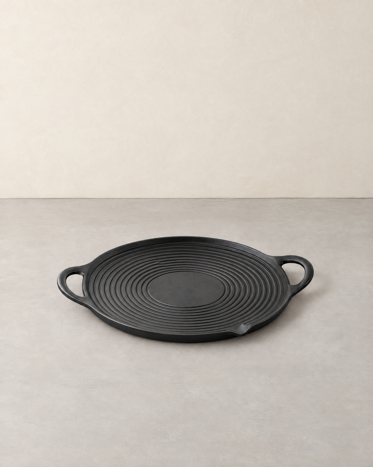 Round black cast iron grill pan with raised rings, two loop handles and an oil spout