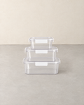 Three clear food storage boxes with white clip lids stacked largest to smallest on a pale concrete floor