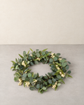 Artificial eucalyptus wreath with clusters of white berries lying flat on a pale grey floor against a cream wall
