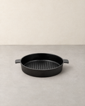 Round black cast iron grill pan with raised ribs and two short tab handles