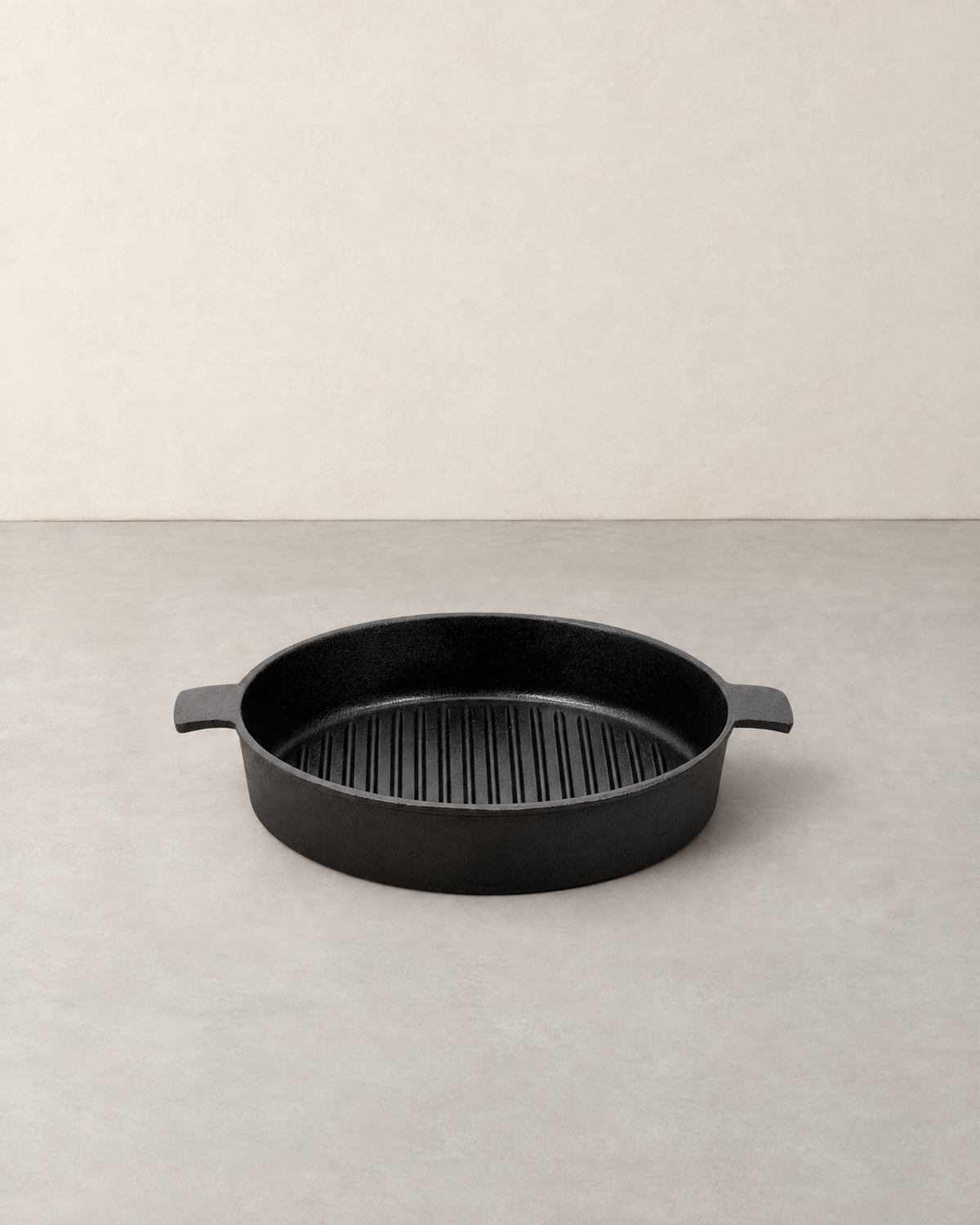 Round black cast iron grill pan with raised ribs and two short tab handles