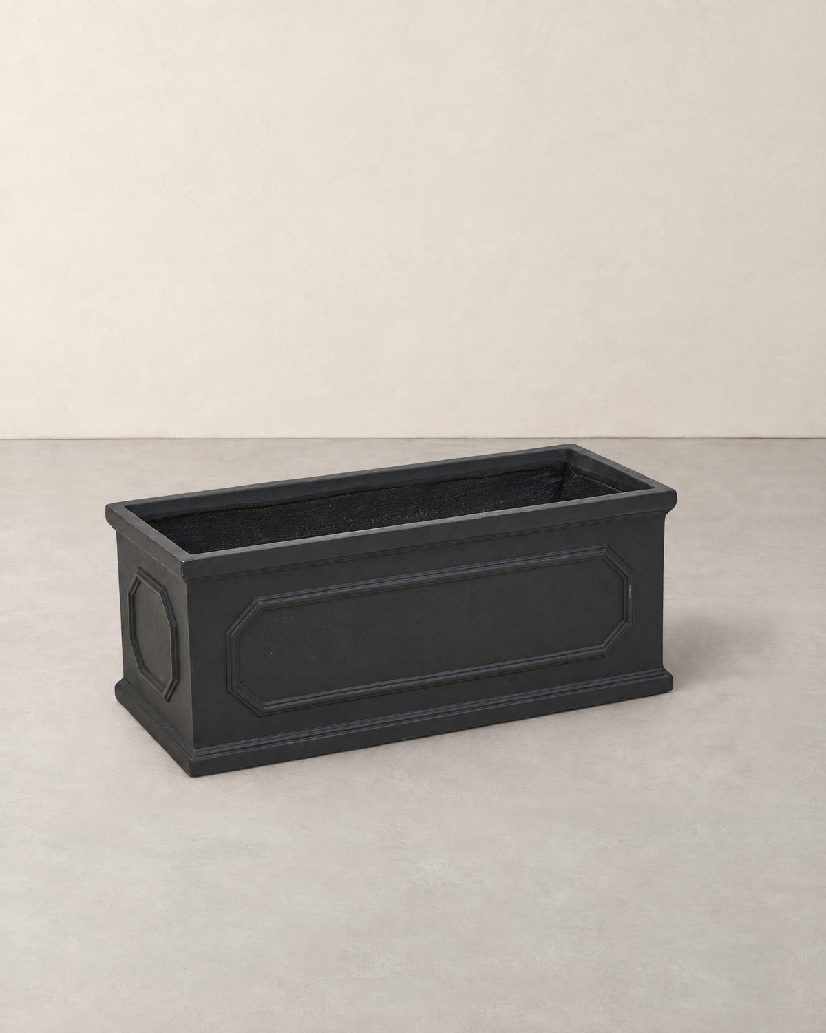 Long black cement trough planter with raised panels on the front and ends, empty
