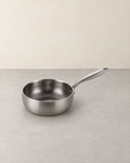 Deep hammered titanium saute pan with a long handle standing empty on a pale concrete floor against a cream wall